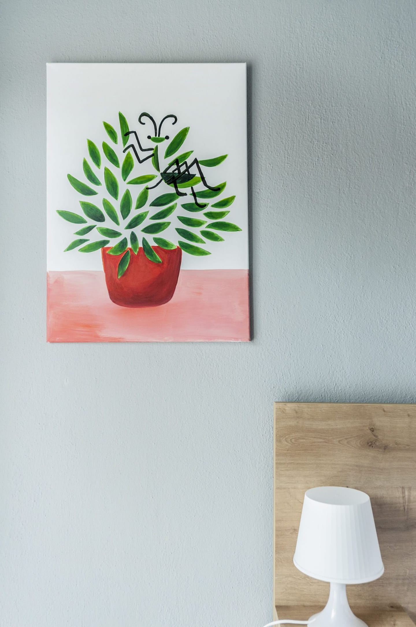 Painting of a plant in a red pot above a bedside lamp